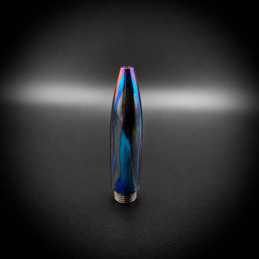 A metallic bullet-shaped pen tip with a dark blue and black base and an iridescent, rainbow-reflective coating, standing upright on a dark, vignetted background.