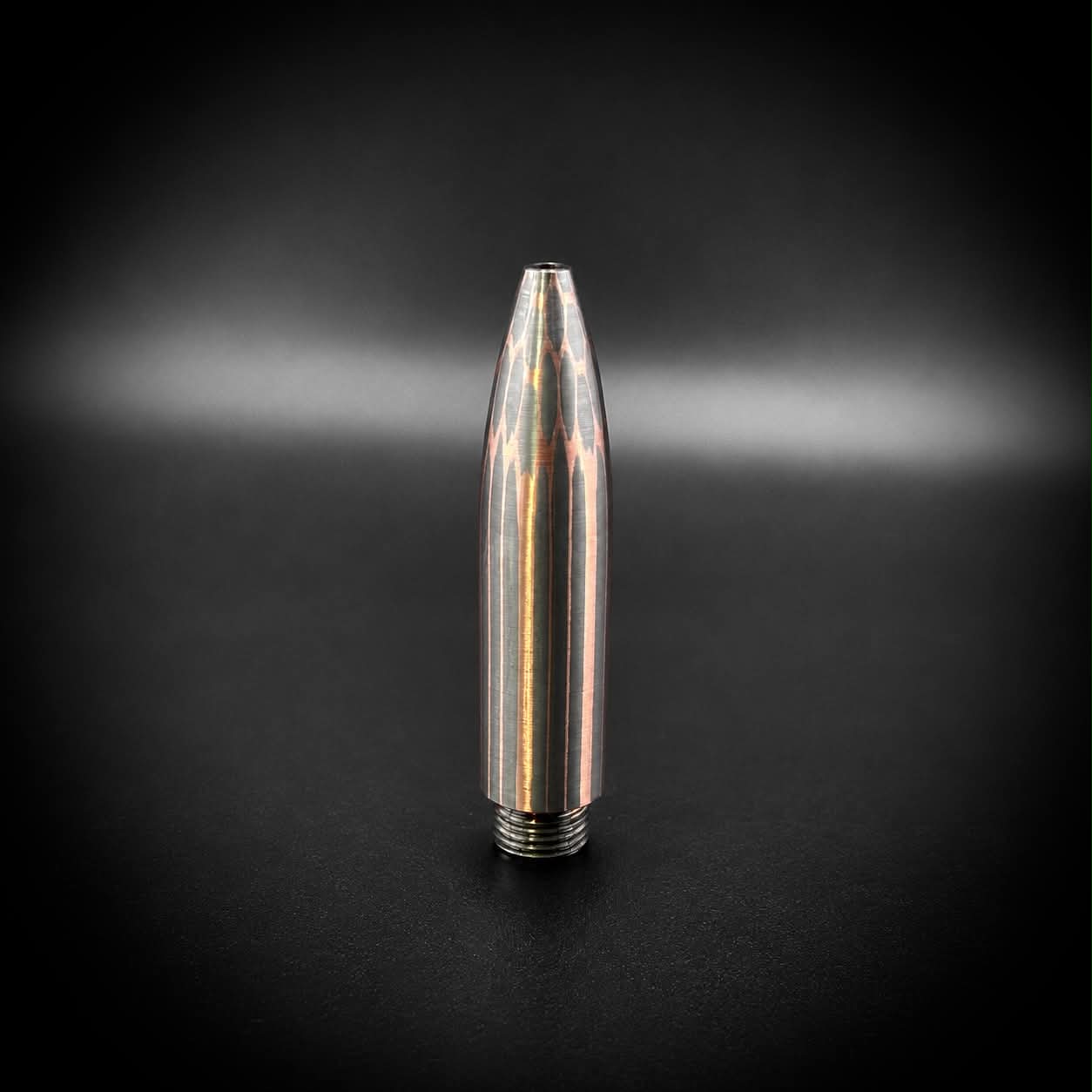 A metallic bullet-shaped pen tip with a threaded base, standing upright on a dark surface against a black background with a soft spotlight effect.
