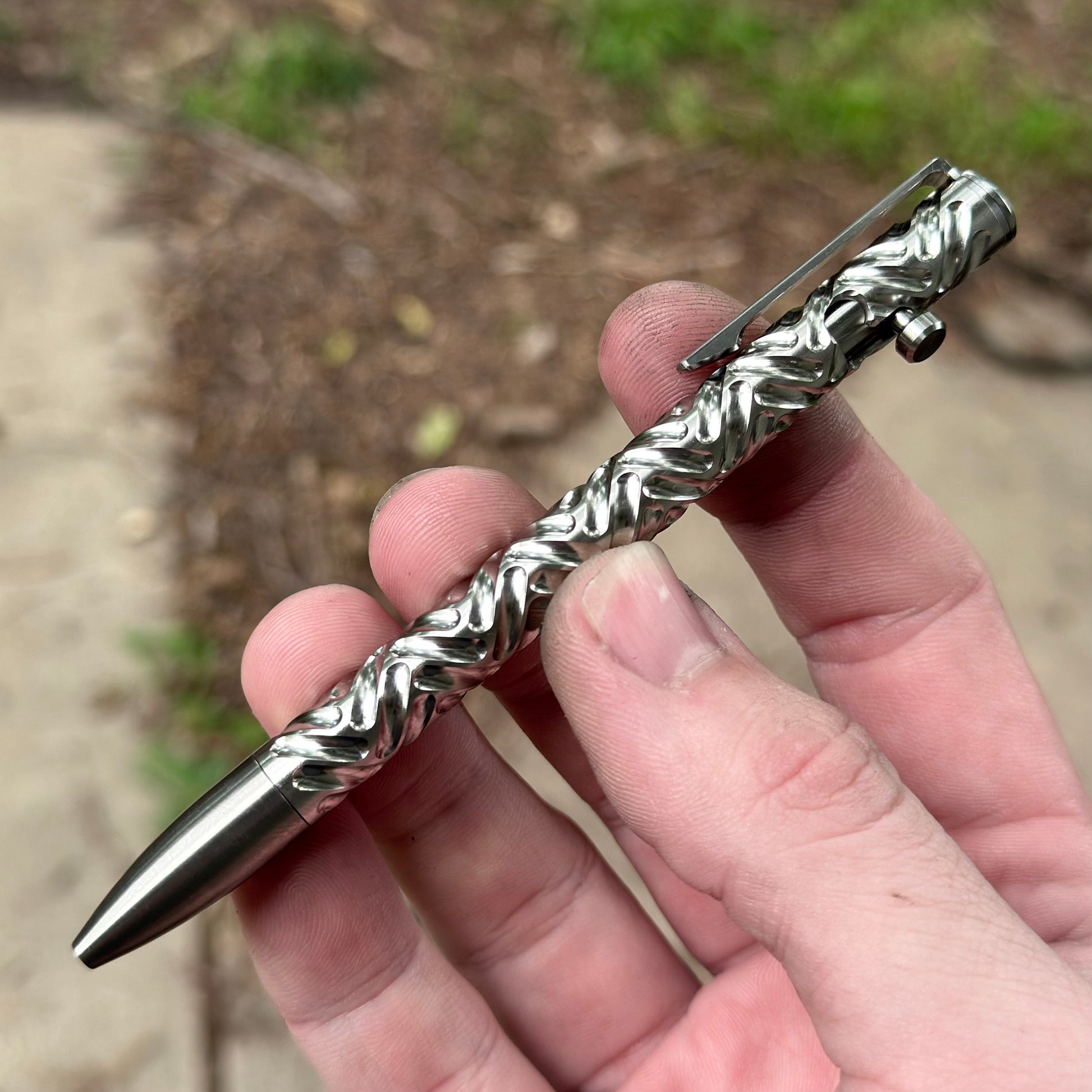 Metallic pen held in a hand with a blurred natural background